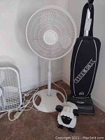 Photo showing Oreck XL Xtended Life upright vacuum, white standing oscillating fan, and wooden sheep doorstop on a carpeted floor.