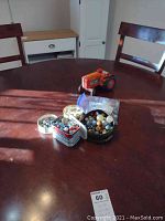 Photo of the full lot on a wooden table with vintage battery-operated orange tractor and three containers of glass marbles