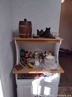 Photo shows a wood and ceramic ice bucket shaped like a barrel with copper bands, a black cast iron boot, and other kitchen and household items on shelves.