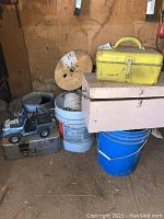Multiple metal pails, two toolboxes, blue plastic bucket, spool of wiring, toy Jeep inside garage