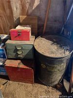 Wide shot showing large metal water drum, green three-drawer tool organizer and two red metal tool boxes on the floor in a garage setting.