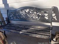 Full view of garden bench with cast iron back and wooden seat slats showing weathering and paint chipping.