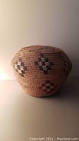 Front view of round basket with lid attached showing geometric motifs on natural straw color