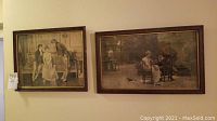 Two framed antique wall art prints hanging on a wall, showing vintage scenes with people dressed in period attire.