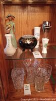 Shelf display of all vases, figurines, flower frog, and champagne glass