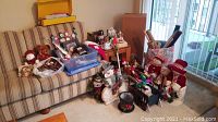 Overview of assorted Christmas decorations including plush snowmen, caroling figures inside and outside a plastic bin, a brown teddy bear, and other holiday decor on and around a striped sofa.