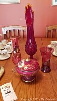 Full view of lot showing cranberry hobnail vase, Limoges candy dish, and two glass vases on table with other items in background.
