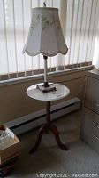Full view of the marble top side table with lamp on top near window.