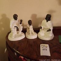 Photo of three porcelain figurines with dark brass-tone faces and hands displayed on wood table.