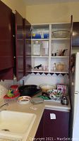 Kitchen corner featuring open cabinets and countertop displaying kitchenware items including large black granite roasting pan, mixing bowls, Brita pitcher, glass juice container and more.