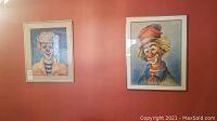 Two framed clown watercolor and pen artworks hanging on a red wall.