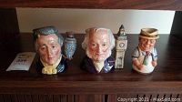 Front view of all four Royal Doulton Toby mugs arranged side by side on a wooden shelf, showing the different character designs.