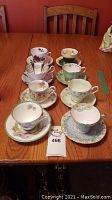 Full set of eight tea cups with matching saucers arranged on table showing variety of floral designs and colors.