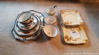 Photo showing Wedgewood Machu cups, saucers, plates, creamer, and sugar bowl beside Myott floral plates and platter on carpet.