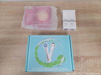 Photo of three boxed items: pink box for FOREO UFO 2 device wrapped in protective mesh, and two white boxes of The Ordinary Hyaluronic Acid 2% + B5 serum bottles, all on a wood surface.