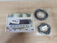 Box of FCAUDIO KM200 sound mixer with knobs and ports visible, two packaged 6.3mm audio cables on the right