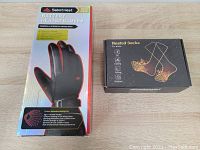 Photo showing front boxes of SabotHeat battery heated gloves and heated socks, both new in packaging.