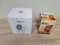 Photo of two boxed heaters on a wooden surface: GAIA Top personal heater and Flame Heater 900W.