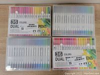 Four boxes of BOIROS 36-color dual tip art markers arranged flat on a wooden surface showing caps colors and semi-transparent cases.