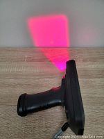 Side view of the handheld MUNBYN barcode scanner showing the grip handle and red scanning light projection on surface.