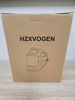 Closed cardboard box packaging labeled HZXVOGEN with a line drawing of welding helmet.