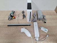 Full set of Wii console accessories arranged around the main console: including one Wii Remote, one Nunchuk, sensor bar, AV cables, power adapter, and HDMI converter.