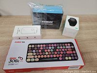 Photo of all four items: AJAZZ keyboard, SEMLOS lamp, label printer D30S, Jelly Comb mouse still in packaging, on wooden table.