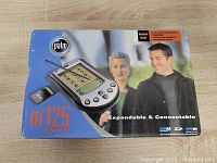 Original box of the Palm M125 handheld PDA showing blue and orange branding and images of the device and connectivity features.