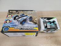 Photo shows two boxed radio control cars: a large Amphibious Radio Control car box with water and dirt graphics, and a smaller radio control stunt car box.