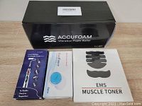 Photo showing four boxed items: EMS Muscle Toner with electrode pad images, Accufoam Vibration Foam Roller box, Electronic Acupuncture Pen in box, Hot & Fancy Cold Pack box.
