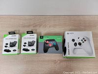 All boxes together on tabletop showing four packaged items including the Xbox Robot White controller, Beexcellent gaming controller, and two Dobe dual charging docks.