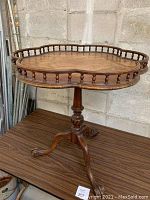 Front side view of antique mahogany wine table showing kidney-shaped top with turned spindle gallery and tripod claw feet base.
