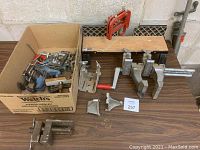 Set of clamps on table including corner clamps with red handles and metal clamps with wooden board clamped