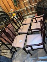 Set of six dining chairs, four armless and two with arms, arranged on concrete floor. Upholstered seats in pinkish fabric and dark wood frames visible.