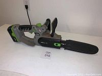 Side view of the cordless rechargeable mini chainsaw displayed on a white surface, showing the ergonomic handle, battery pack, and protective sheath on the blade.