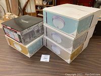 Five boxed flush mount lighting fixtures stacked on a table, showing four sealed boxes and one open box.