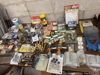 Overview of assorted household hardware laid out on table including door knobs, adhesive pads, L brackets, packaged hardware items, and small tools.