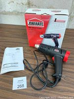 Image of Jobmate heat gun with power cord, instruction manual, and original box on wooden surface.