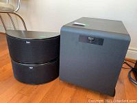 Two half-moon shaped ICON-VS14 surround speakers next to SW-450 subwoofer on floor