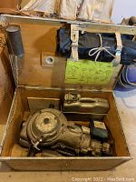Opened wooden case showing motor drill, fuel tank and tool roll strapped to lid