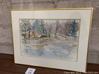 Framed and matted watercolour painting of a lakeside landscape with trees, behind glass.