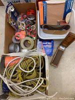 Photo of ropes in white and twisted yellow lying inside a white tray along with sandpaper belts and a wooden box containing additional small tools or sandpaper.