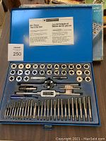 Open blue plastic case showing all 60 pieces laid out in foam insert with threading dies, taps, and threading handles visible.