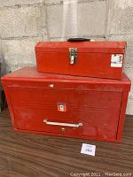Two red metal toolboxes stacked: smaller toolbox on top with some visible wear, larger toolbox below with minor scratches and silver handle