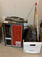 Welder unit with attached power cable, welding helmet and box of rods arranged on floor