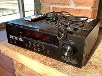 Front-left angled view of Yamaha AV receiver with remote and power cable on top, showing volume knob and front panel buttons.