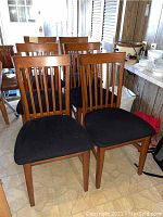 Six wooden dining chairs, medium brown finish, black upholstered seats, vertical slat backs shown grouped together.