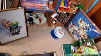 Photo showing framed Disney posters including Mickey Mouse, wooden toy vehicles, colorful block toys, and Disney memorabilia such as plates and caps arranged in a corner.