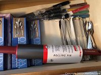 Drawer with boxed Oneida flatware sets and KitchenAid rolling pin.