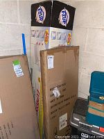 Photo showing the original boxes of the E-Z Up instant shelter and the convertible step ladder to hand truck stacked against a wall.